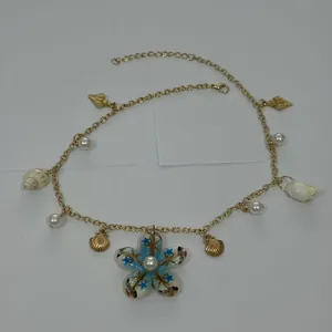 Dettaglio della collana dorata in stile spiaggia con conchiglie e ciondolo fiore.