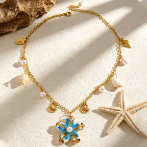 Dettaglio di collana dorata stile spiaggia con ciondolo a fiore blu e conchiglie.