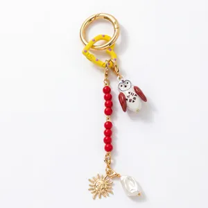 Porte-clés DIY bohème avec hibou, soleil, perles rouges et nacre sur fond blanc épuré
