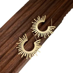 Gold sunburst fan-shaped hoop earrings displayed on a dark wooden textured block