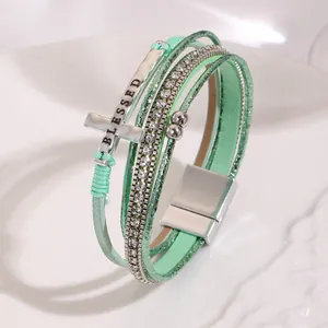 Close-up of bohemian multilayer leather bracelet with cross and BLESSED engraving