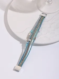 Detailed view of a blue multi-layered leather bracelet with a rhinestone cross charm.