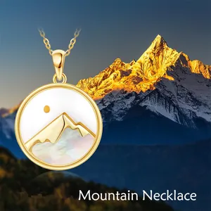 Detailed close-up of a gold mountain pendant necklace against a scenic mountain backdrop