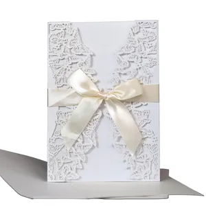 Laser-cut white wedding invitation card with butterfly pattern and cream ribbon bow