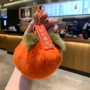 Close-up of a plush orange persimmon keychain featuring a red tag with lucky text.
