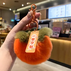 Close-up of a fuzzy orange persimmon plush keychain with a green leaf top and tag.