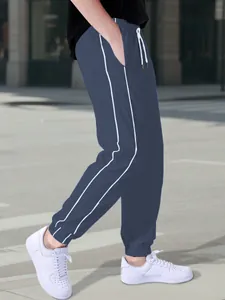 Side view of men's navy blue parachute joggers with white side stripes and elastic cuffs.