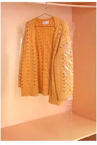 Transparent plastic clothing dust cover hanging with yellow sweater in a wooden wardrobe