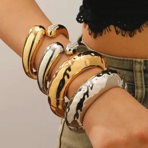 Detailaufnahme von klobigen gold- und silbernen Hammerschlag-Armreifen am Frauenarm