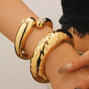 Nahaufnahme eines massiven, gehämmerten goldfarbenen Armreifs und Kristall-Armbands