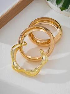 Detail of three-piece gold bracelet set featuring irregular wavy open cuff design