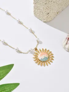 Detailed view of gold sun pendant with pink and blue wave enamel on pearl chain