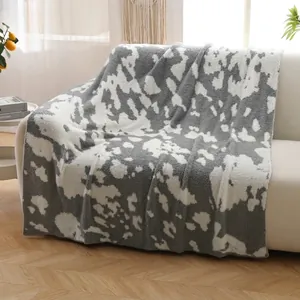 Thick cow print flannel throw blanket draped over a modern sofa in a cozy bright room
