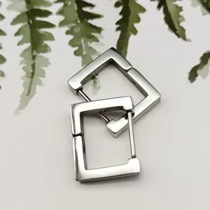 Close-up of minimalist silver rectangular titanium steel hoop earrings on leaf background