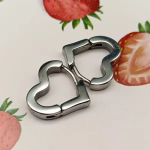 Close-up of polished silver heart-shaped titanium steel hoop earrings on strawberry print