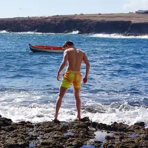 Outdoor lifestyle shot of man wearing color-changing yellow swim trunks on rocky beach
