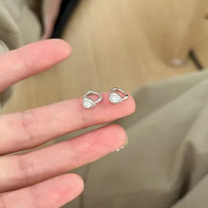 Dainty silver heart-shaped zircon hoop earrings held on fingers for scale display