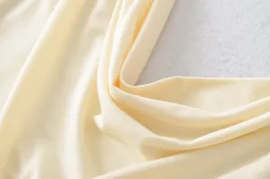Macro detail of soft pale yellow ribbed knit fabric showing fine texture and elegant draping.