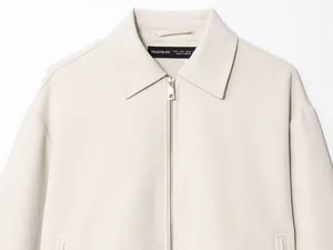 Detailed macro view of a minimalist beige zip-up jacket collar and metal zipper