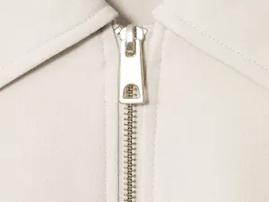 Macro view of a high-quality metal zipper on a stylish beige women's fashion jacket.