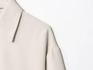 Detail shot of a minimalist beige women's jacket showing collar and shoulder seam texture.