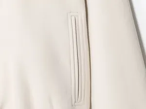 Detailed close-up showing the vertical welt pocket design on a beige fashion jacket.