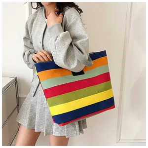 Model carrying a large colorful striped canvas tote bag in a minimalist setting