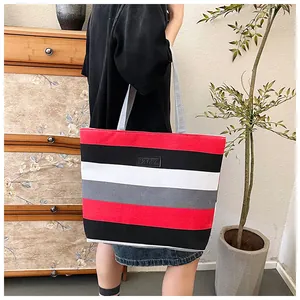 Large striped canvas tote bag carried by a model in a stylish indoor lifestyle setting