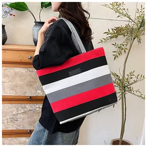 Woman carrying a large canvas tote bag with bold red and black horizontal stripes