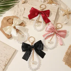 Detailed view of four colorful bowknot pearl keychains on a sandy beach background.