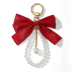 Close-up of a red satin bow keychain with elegant white faux pearl charms and gold clip.