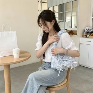 Woman holding a blue and white striped pleated shoulder bag with bow details in a cafe