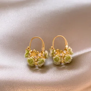 Close-up detail of gold flower basket earrings with pale green roses and zircons