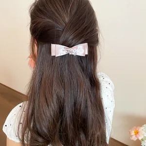 Detail view of pink silk bow hair clip with crystal flower on brown hair
