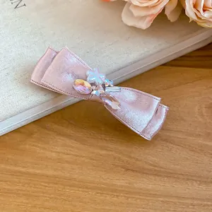 Close-up detail showing the rhinestone and pearl accents on a pink satin bow hair clip