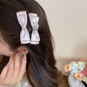 Detail of pink fabric bow hair clip with pearls and rhinestone flower worn on hair.