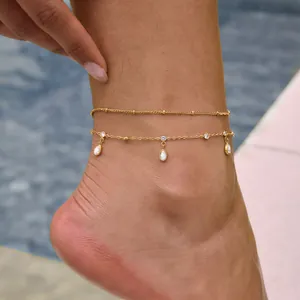 Primer plano de una tobillera de doble capa bañada en oro de 18k con elegantes dijes de circón.
