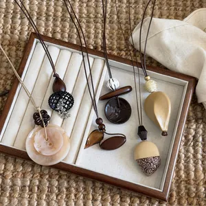Detail view of five Maillard style irregular long necklaces with wooden pendants on tray