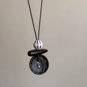 Close-up of artistic Maillard style necklace featuring textured dark beads and pendant