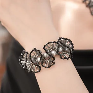 Détail d'un bracelet artisanal en perles de verre noires avec des perles argentées au poignet.