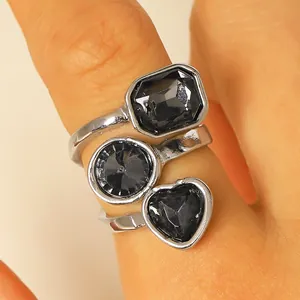 Anello argentato con tre pietre nere sfaccettate a forma di cuore, cerchio e rettangolo.