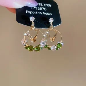Gros plan de boucles d'oreilles créoles papillon Monet Garden avec cristaux verts.