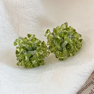 Vue détaillée de boucles d'oreilles fleurs en zircone verte sur tissu blanc texturé.