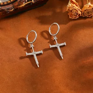Nahaufnahme eleganter Silber-Kreuzohrringe mit glitzerndem Zirkonia auf braunem Grund.