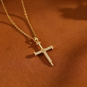 Detailansicht einer goldenen Kreuzkette mit Nageldesign und funkelndem Zirkonbesatz