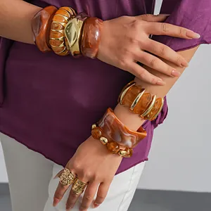 Gedetailleerde weergave van retro amber acryl armbanden en gouden ringen op de arm van een model.