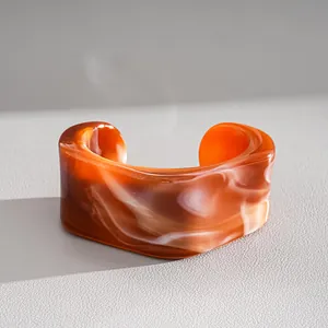 Detailopname van onregelmatige geometrische acryl manchetarmband met oranje marmerpatroon