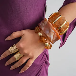 Detailweergave van onregelmatige geometrische marmeren acryl armbanden en gouden ringen op model.