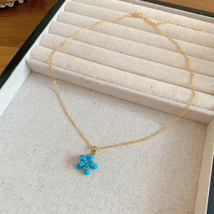 Dettaglio di una collana placcata oro 18k con ciondolo a fiore blu in un vassoio per gioielli.