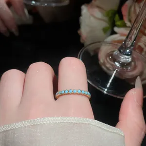 Vista dettagliata di un elegante anello eternity in oro con pietre turchesi sul dito